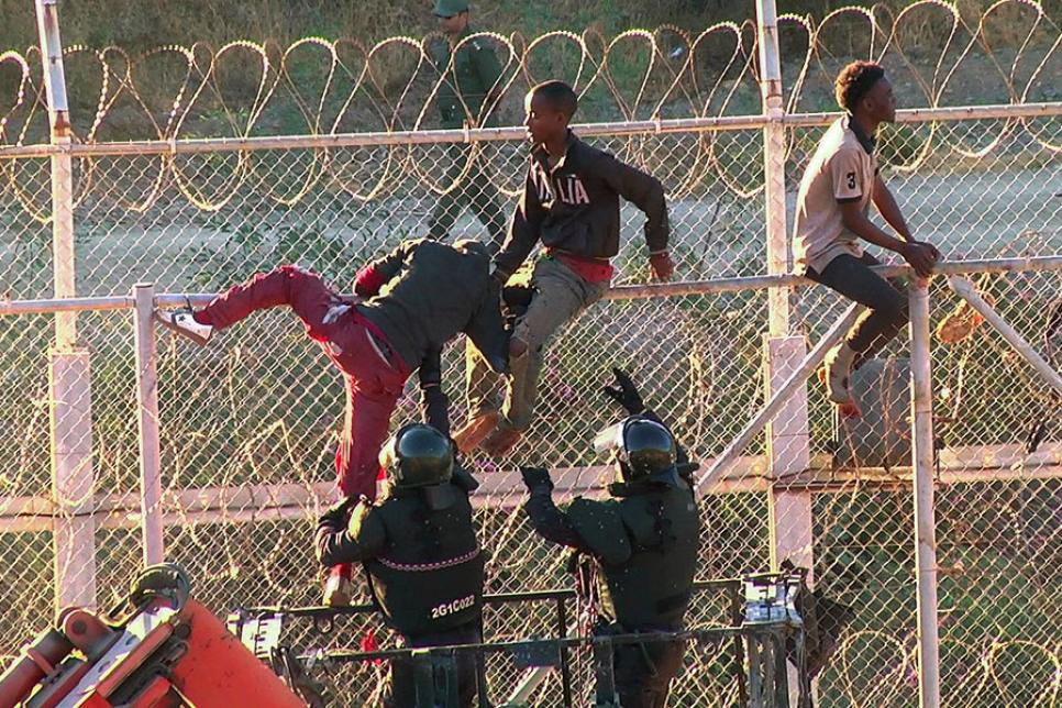 Мигранты, перелезающие через колючую проволоку в Испании